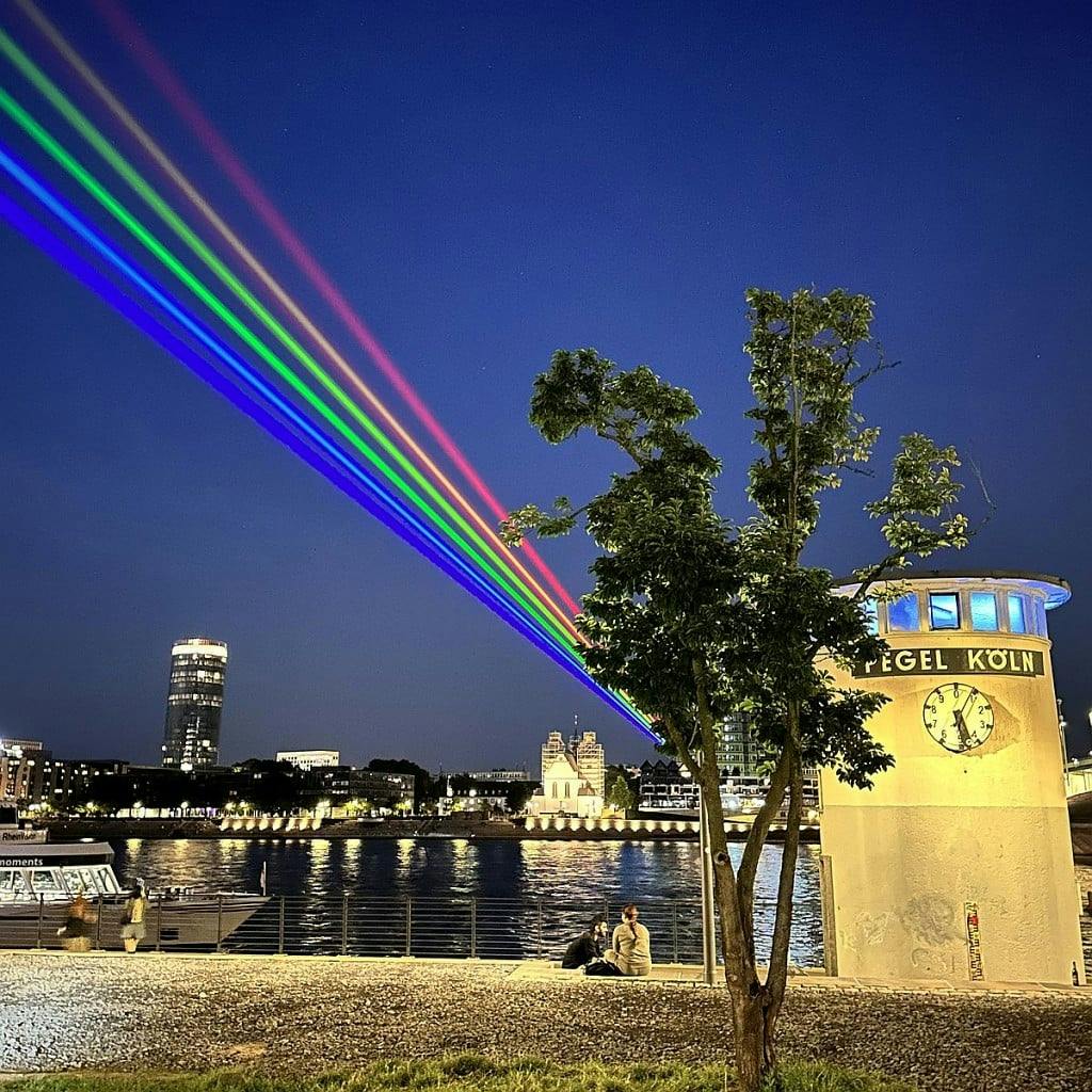 Ab Donnerstagabend leuchet mit Einbruch der Dunkelheit ein riesiger Laser-Regenbogen über Köln.  
