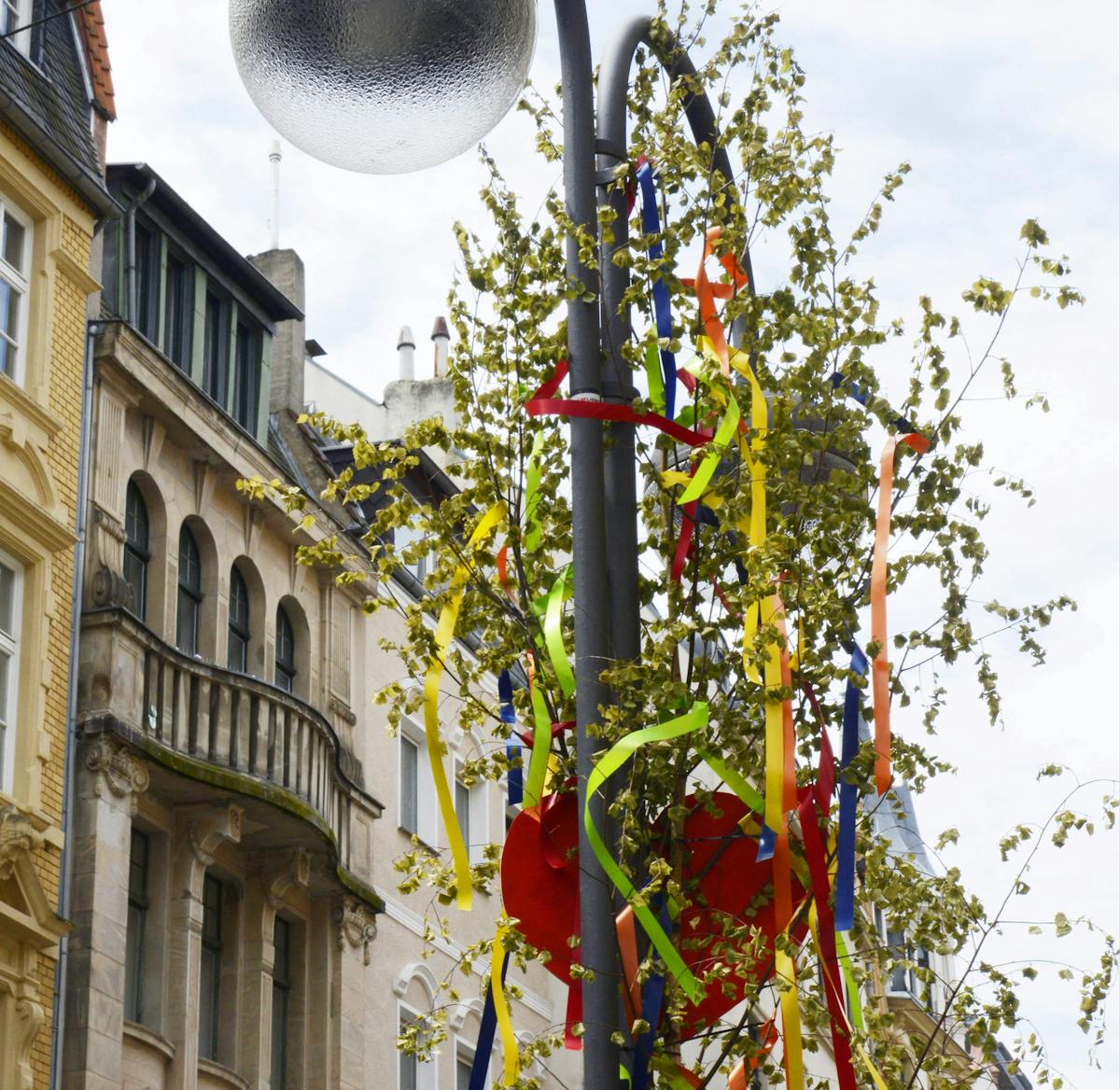 Ein Maibaum, geschmückt mit bunten Bändern, ist in Köln an einem Laternenmast befestigt